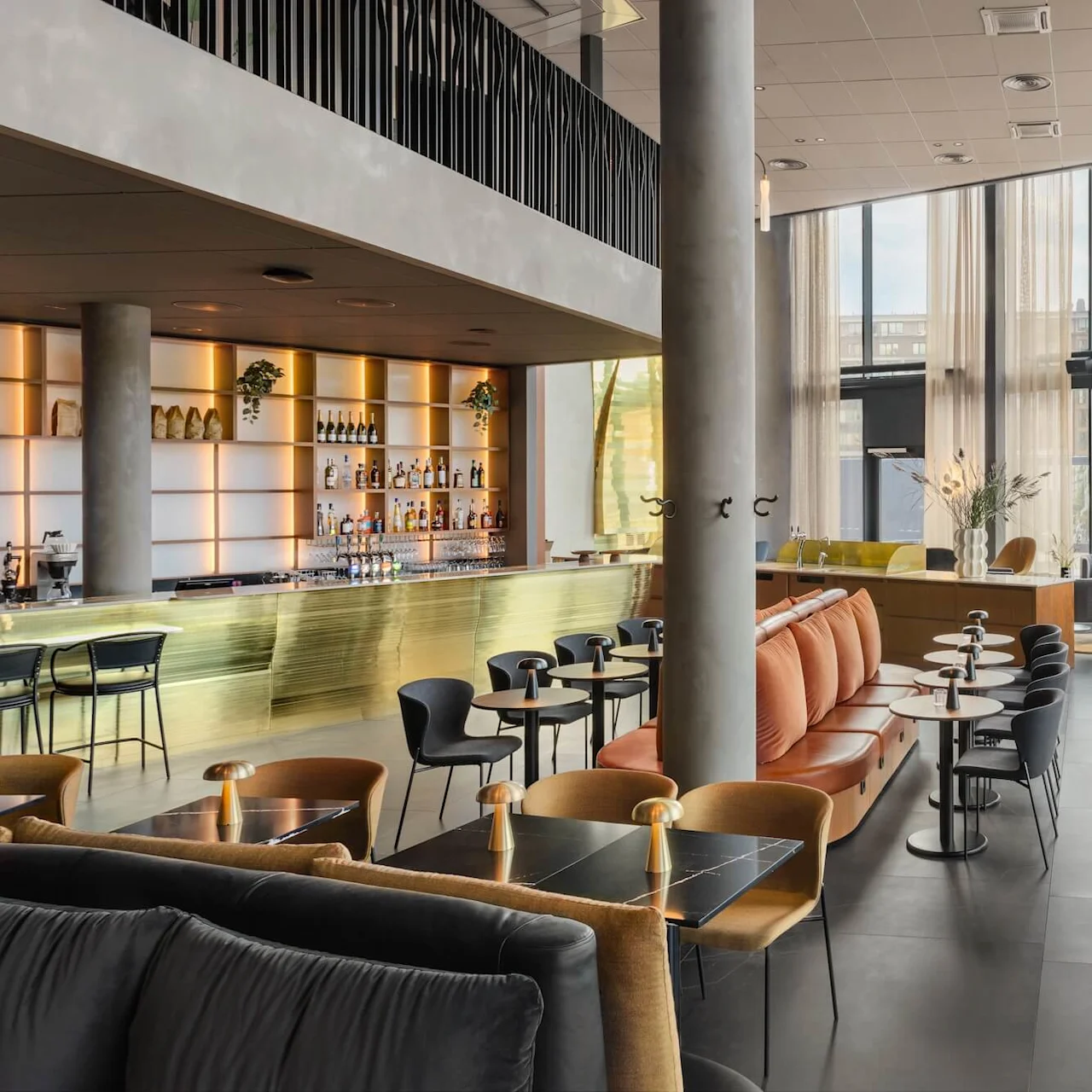 Ett rymligt, modernt loungeområde med eleganta sittplatser och en elegant bar med hyllor fyllda med drycker. Stora fönster ger naturligt ljus, medan växter och dekorationer skapar en inbjudande atmosfär.