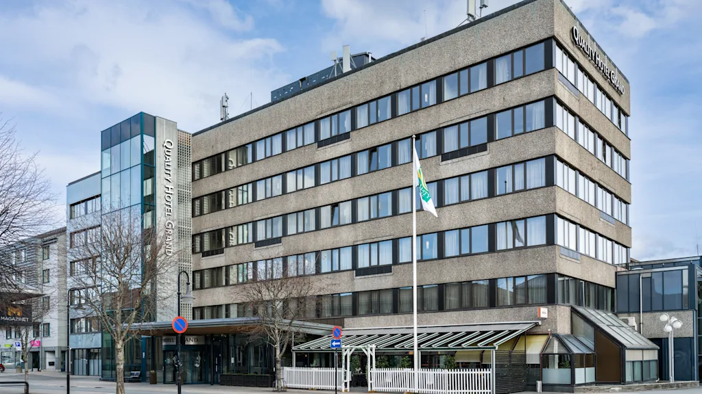 Et fleretasjes hotellbygning står stille ved en bygate; skiltet lyder "Quality Hotel Maritim", med flagg blafrende i nærheten under en blå himmel.