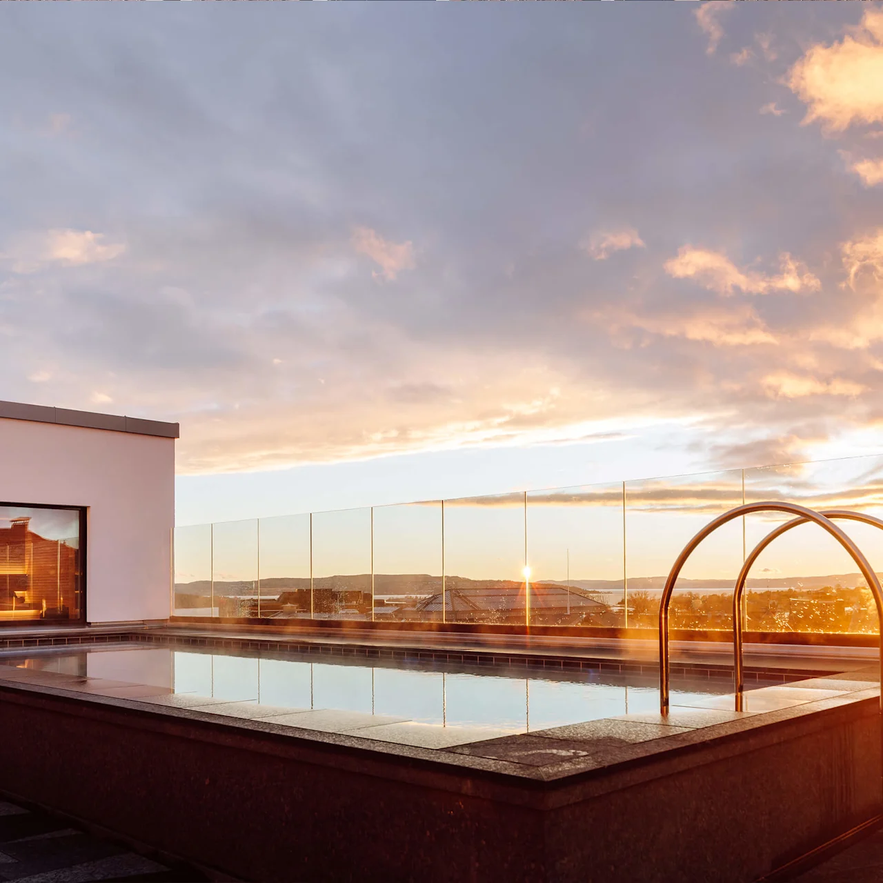 Tagterrasse med pool ved solnedgang med klar udsigt til horisonten og farverige skyer.