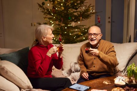 Ett äldre par sitter i soffan och dricker glögg under julen.