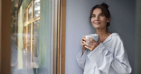 kvinna står vid ett fönster och håller i en kaffekopp