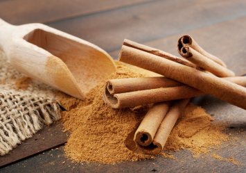 Cinnamon sticks and ground cinnamon powder on a wooden surface, illustrating ingredients that dog owners may wonder about feeding to their pets, addressing the question "Can dogs eat cinnamon?" and the safety of cinnamon for dogs.