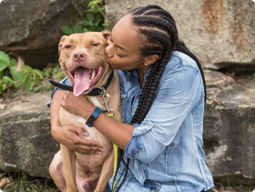 African-American woman hugging and kissing pitbull dog