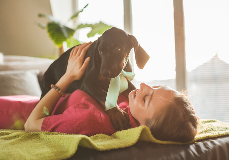 A young woman shares a tender moment with her dachshund puppy on a sunny couch, the kind of sweet scene that makes choosing girl puppy names such a delightful experience.