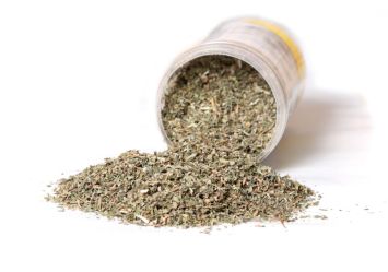 A close-up of a dried catnip herbs spilling out of a jar onto a white surface, commonly used for cats.