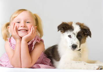 Smiling blonde girl in pigtails posing with a playful black-and-white puppy, perfect for inspiring funny dog names based on their adorable and joyful expressions.