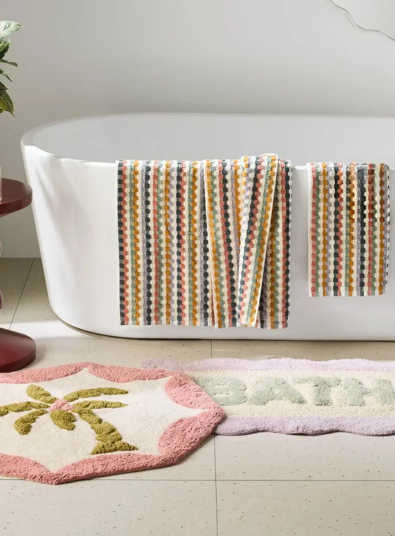 Bath tub with multi coloured bath and hand towel with bath mats on the floor