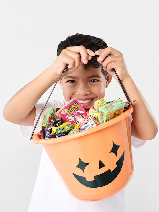 A kid holding a halloween trick or treat bucket filled with c