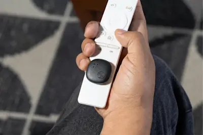 A Life360 Tile Sticker - Black placed on a white television remote.