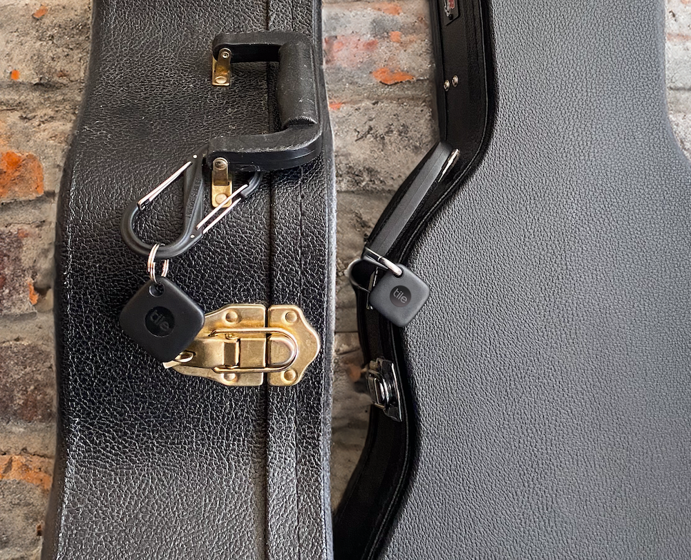 Two Black Tile Bluetooth Mate trackers attached to two black guitar cases on top of a beige and orange rug.