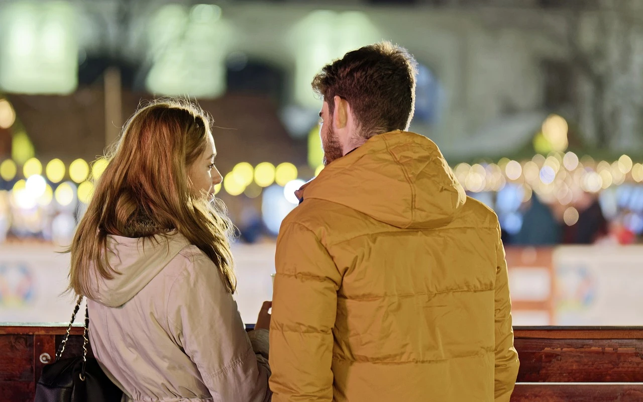 A young couple wearing jackets standing with their backs facing the camera