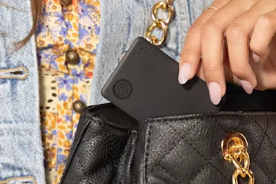 A Life360 Tile Slim Black being placed inside woman's purse. 