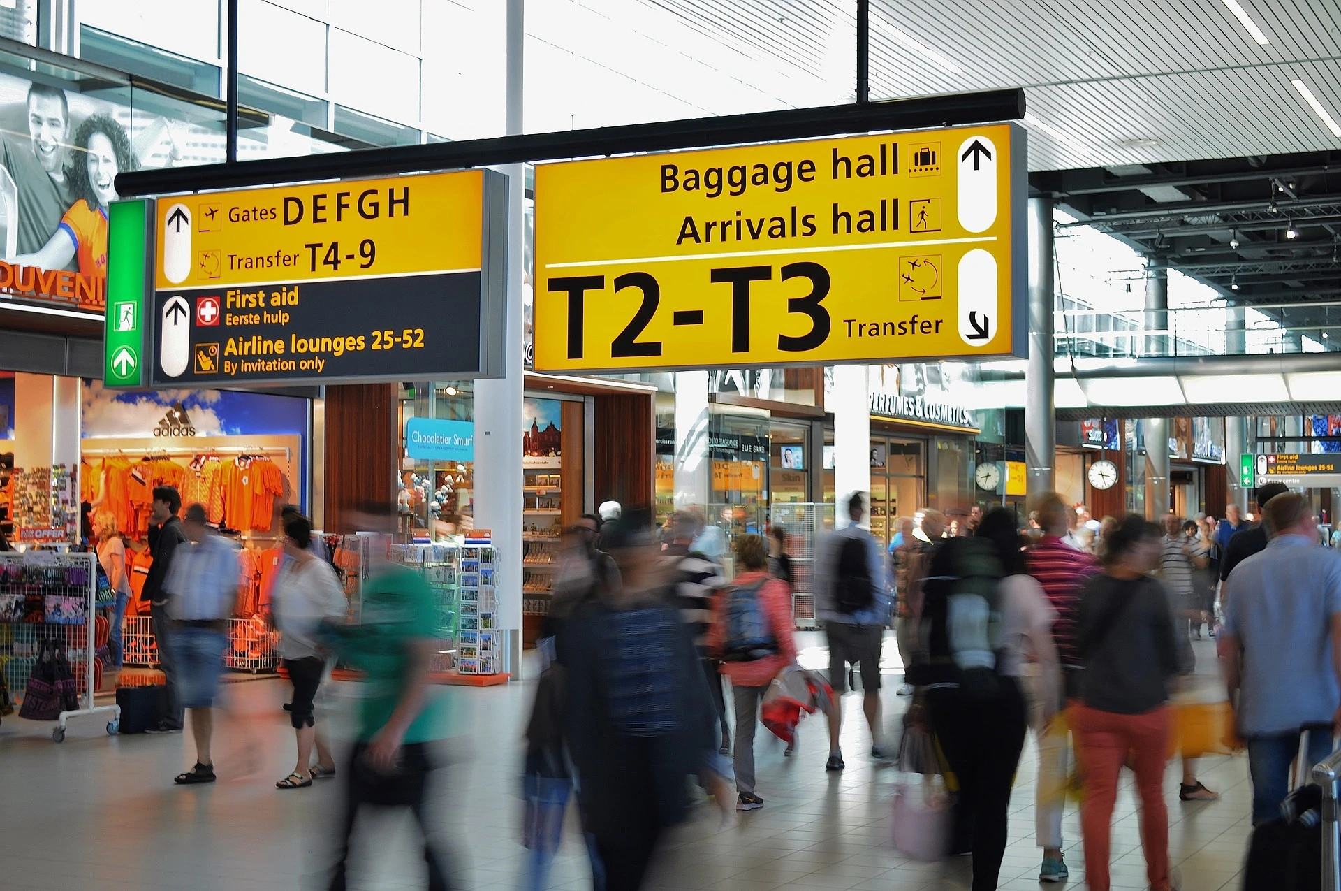 People walking through airport past a sign toward gates and baggage claim