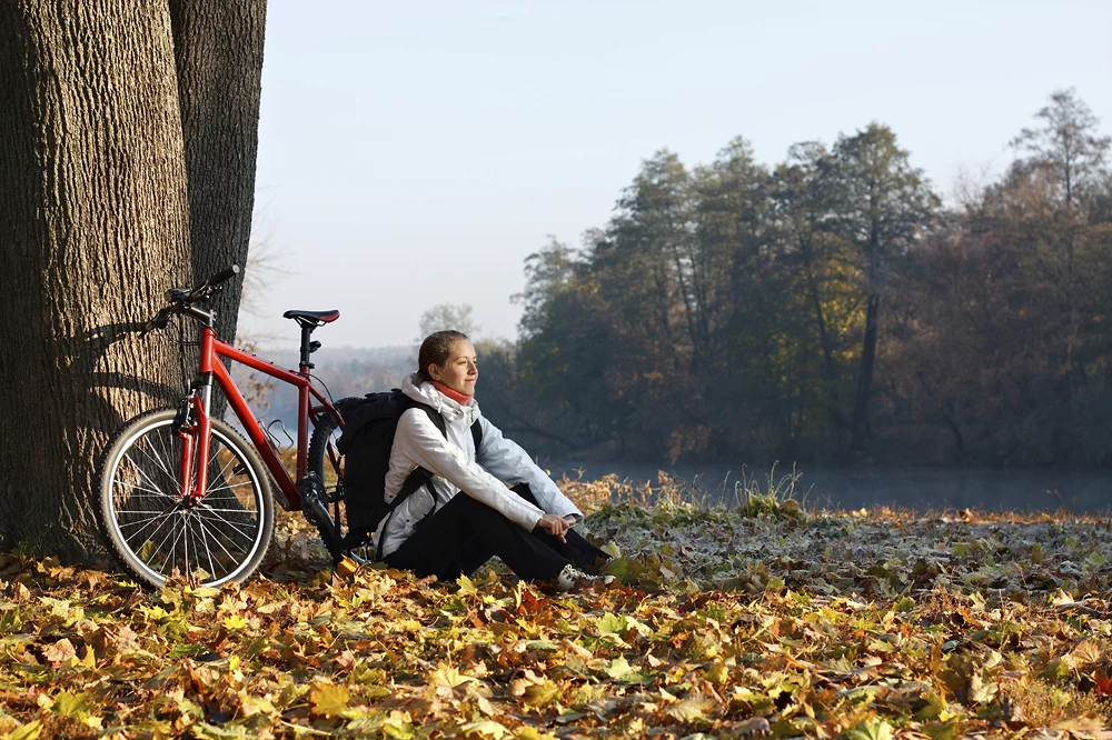 A person sitting under a tree with their bike in fall foliage