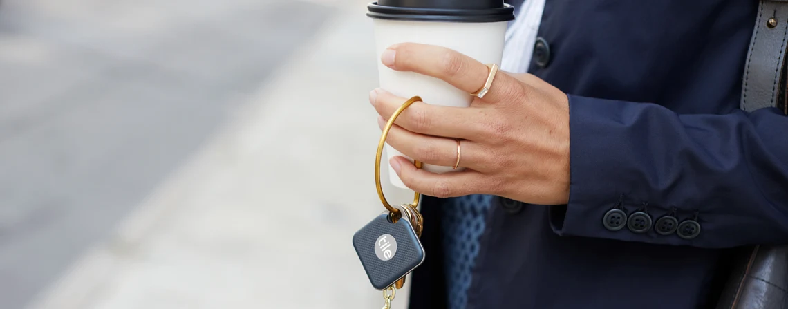 A person holding a coffee and keys with a Tile attached