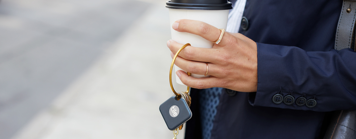 A person holding a coffee and keys with a Tile attached