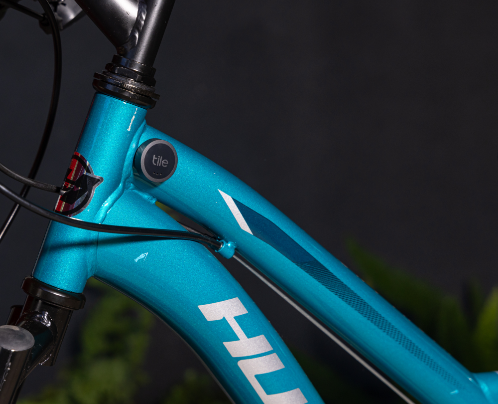 A Black Tile Bluetooth Sticker tracker attached to a bright blue bike with white text against a dark background.