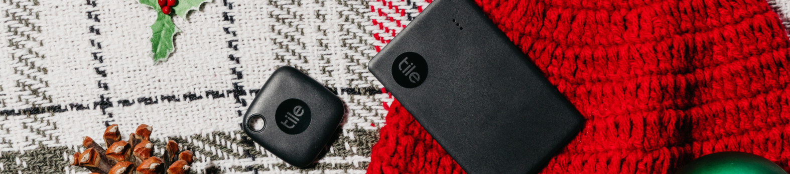 A Black Tile Bluetooth Mate and Slim against a red sweater next to mistletoe against a white and black quilt.
