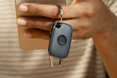 A person holding their phone and keys with a Life360 Tile Pro attached to it.