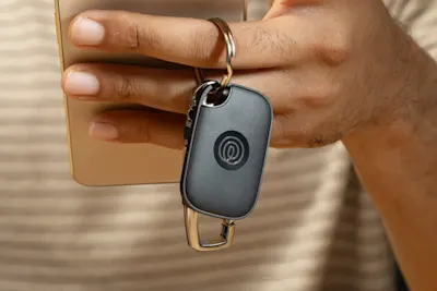 A person holding their phone and keys with a Life360 Tile Pro attached to it. 