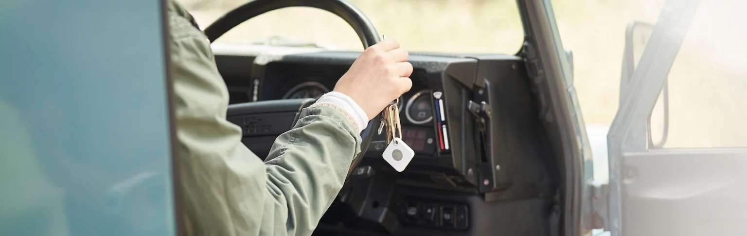 A person at the wheel of a car with a Tile mate attached to their keys