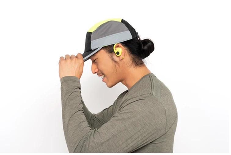 A side profile shot of man in athletic wear wearing yellow bluetooth earbuds with Tile Finding technology built-in.
