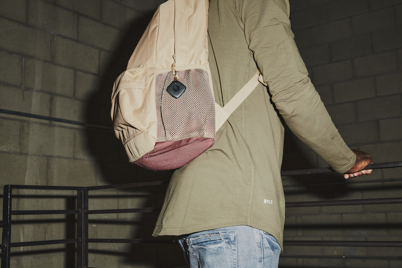 A person wearing a backpack with a Black Tile Mate attached to the side