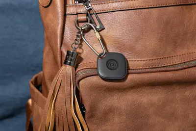 A Life360 Tile attached to brown backpack.