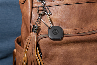 A Life360 Tile attached to brown backpack.