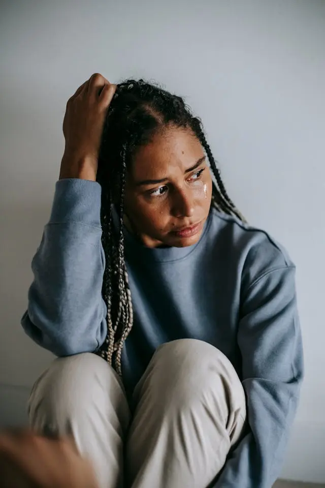 A Black woman sitting on the floor with tears on her face, staring into the distance.
