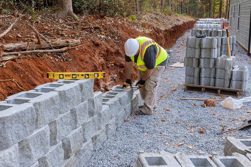 There_was_worker_on_construction_site_installing_concrete_block_for_retaining_wall_near_new_house_that_was_being_built