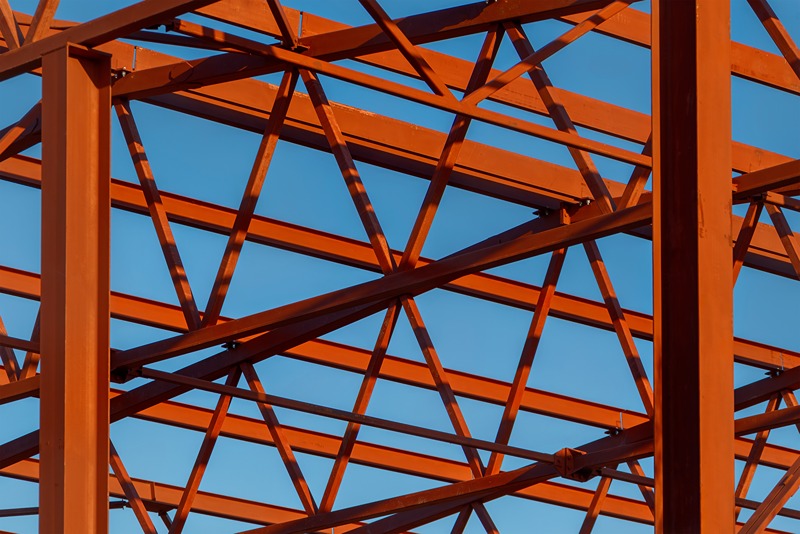 long_red_steel_truss_bridge_spanning_across_a_river_in_a_green_forested_area