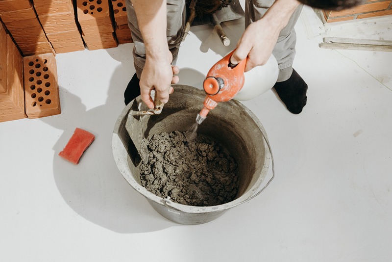 worker_using_an_electric_mixer_to_mix_concrete_in_a_bucket_for_construction