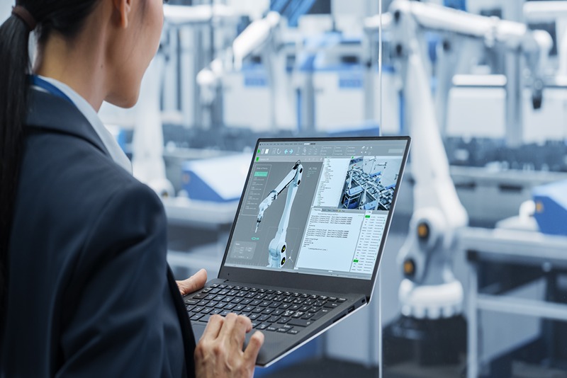 female_engineer_using_laptop_to_monitor_robotic_automation_processes_in_smart_factory_environment