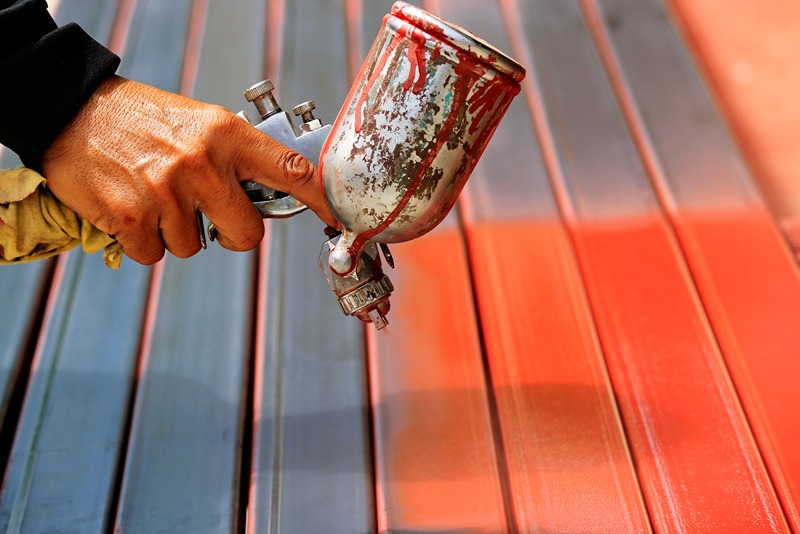 close_up_of_hand_using_spray_gun_to_apply_red_coating_on_steel_panels