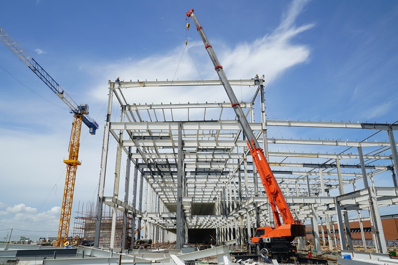 Structure_building_of_steel_structure_roof_truss_frame_installation_by_mobile_crane_under_the_construction_building_in_the_factory_with_blue_sky