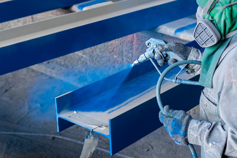 worker_in_blue_helmet_applying_protective_coating_on_steel_surface_in_industrial_construction