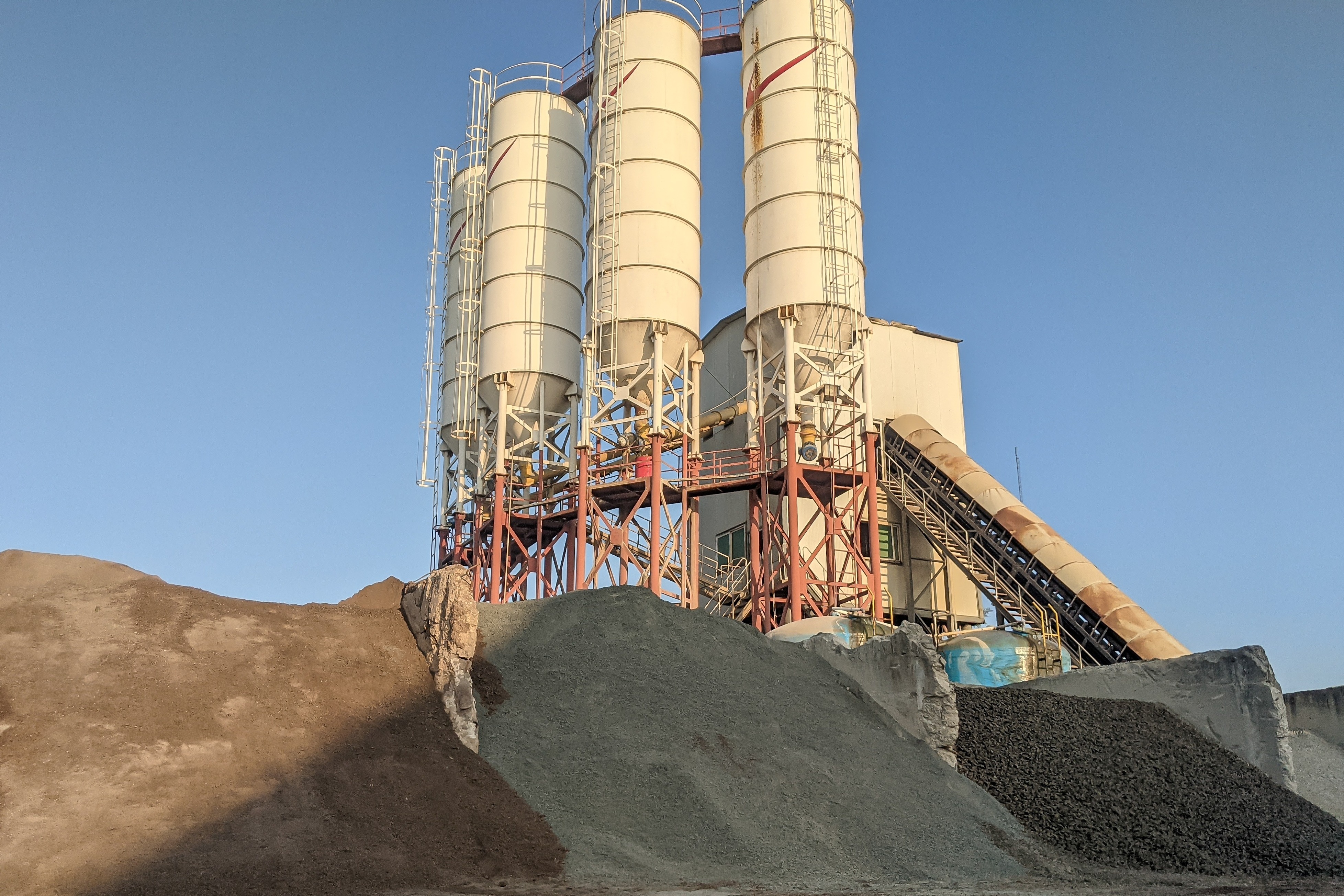 Large_cement_manufacturing_plant_with_heavy_machinery_and_stacks_of_aggregates.