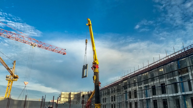 Yellow_crane_is_lifting_a_part_of_pre-cast_cement_wall_to_the_top_of_building_at_condominium_construction_site