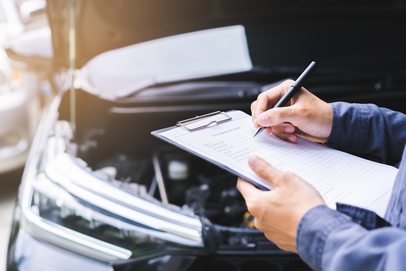 mechanic_inspecting_car_with_clipboard_near_open_hood