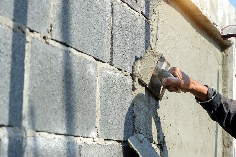 person_applying_a_layer_of_concrete_on_a_wall_surface_with_a_trowel_for_construction