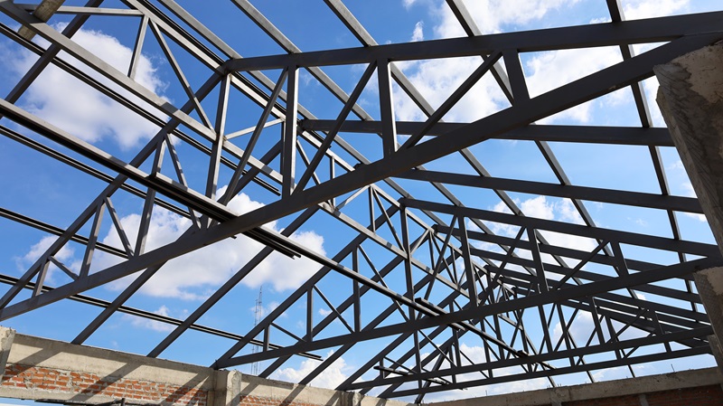 Steel_roof_structure_for_building_construction._Metal_roof_structure_of_a_building_under_construction_on_a_blue_sky_background_with_white_clouds._Selective_focus</br>