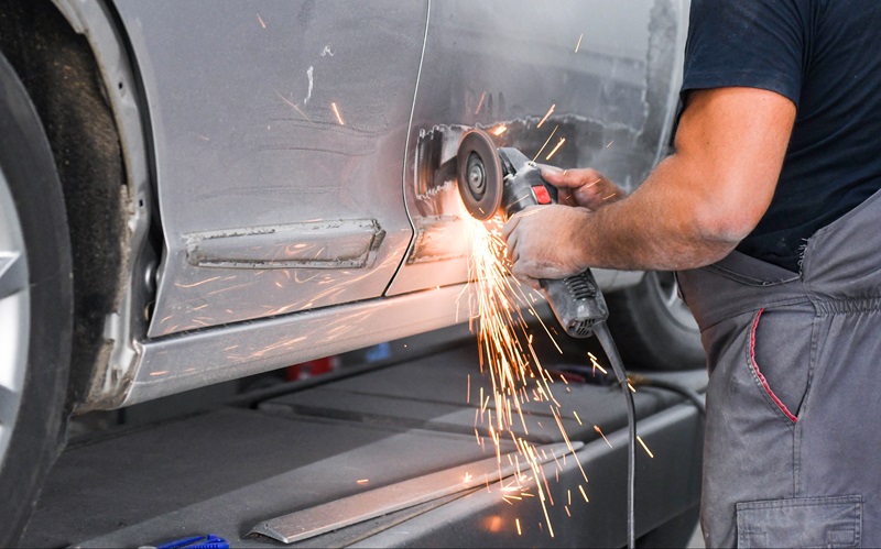 Repair_service_worker_fix_damaged_car._Working_with_angle_grinder_to_fix_metal_body.