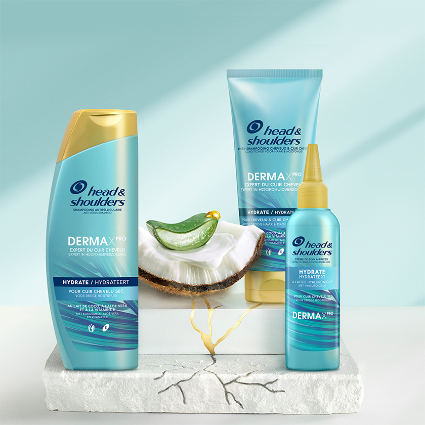 Derma X Pro Hydrateert Head & Shoulders shampoo, conditioner en hoofdhuidbalsem flessen, naast stukjes aloe vera en kokosnoot