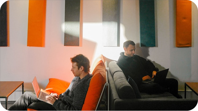 Co-workers sitting on office couches working on their laptops