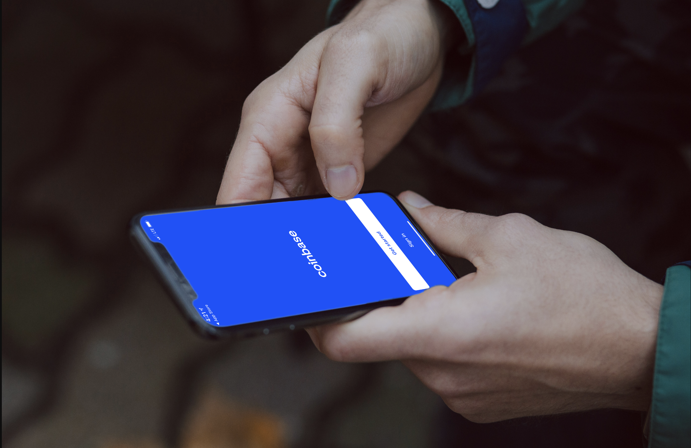 Hand using a mobile phone showing a Coinbase login screen