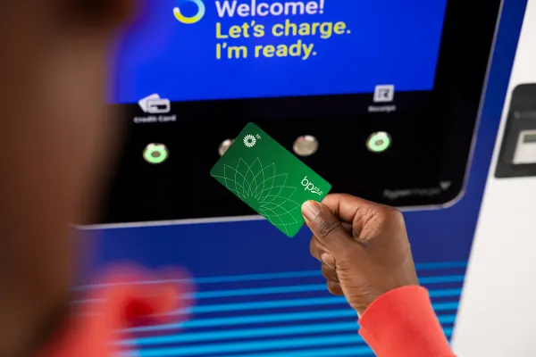 A hand is tapping a green BP Plus card to a bp pulse ev charger.