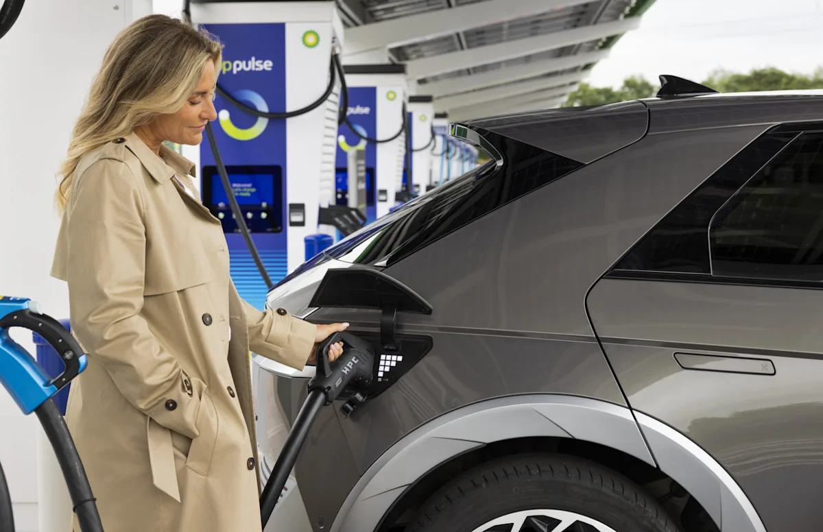 A woman smiles as she plugs her grey electric vehicle in to charge at a bp pulse charging unit. 