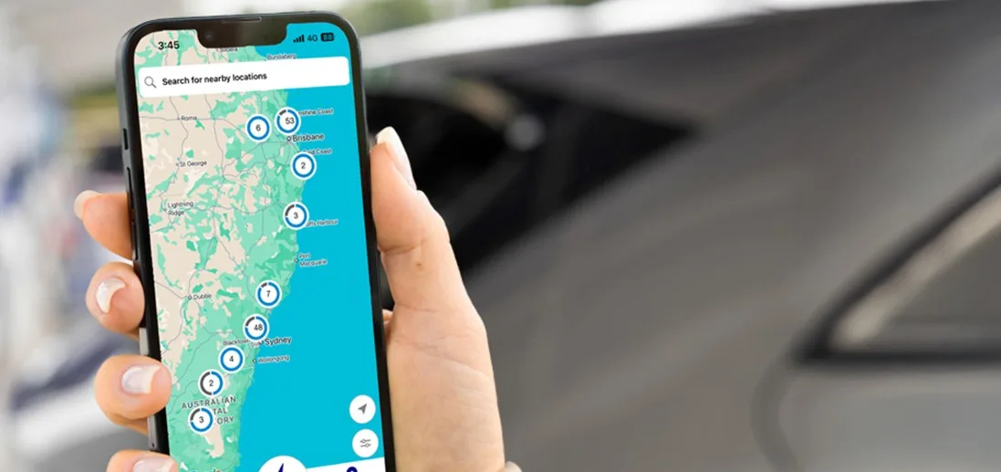A smartphone displaying the bp pulse app with a map of nearby electric vehicle charging locations, held in front of a parked car.