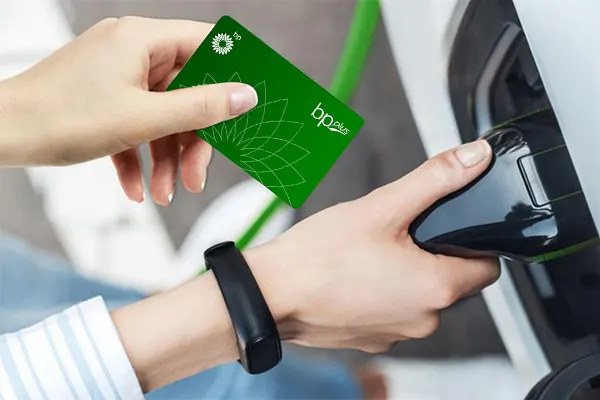 A hand holds a bp plus card whilst the other hand holds an ev charger connector. 